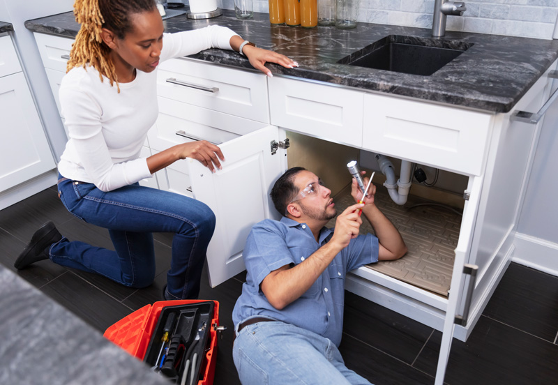Plumber working under the sink while home owner watches